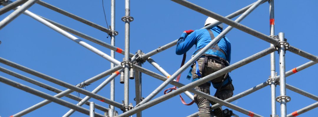 Construction worker working on scaffolding. Steeplejack on the background of clear blue sky